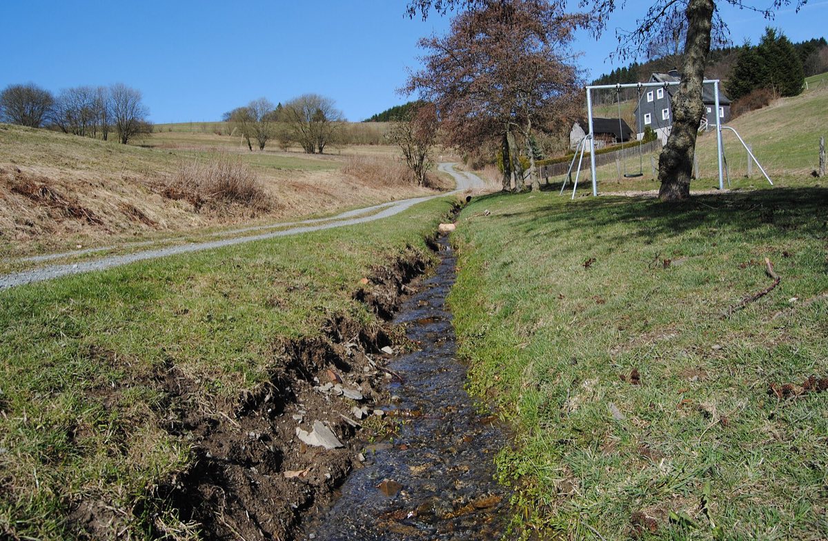 Bach am Haselnußweg in Willingen, daneben eine Wiese mit Kinderschaukel